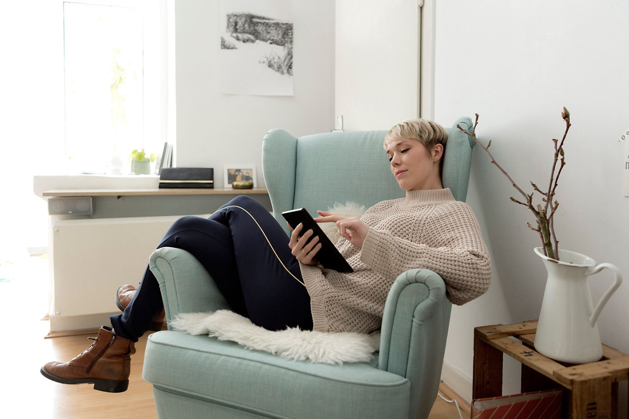 Frau liegt auf einem Sessel mit einem Tablet in der Hand.