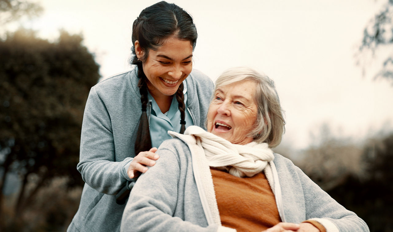 Seniorin und Pflegerin unterhalten sich draußen in der Natur