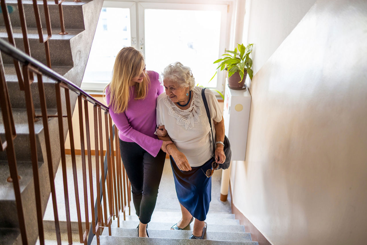Frau begleitet ältere Dame die Treppe hoch