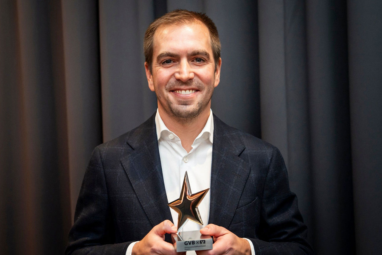 Ein Mann im Anzug lächelt in die Kamera und hält stolz eine Auszeichnung in Sternform in den Händen.