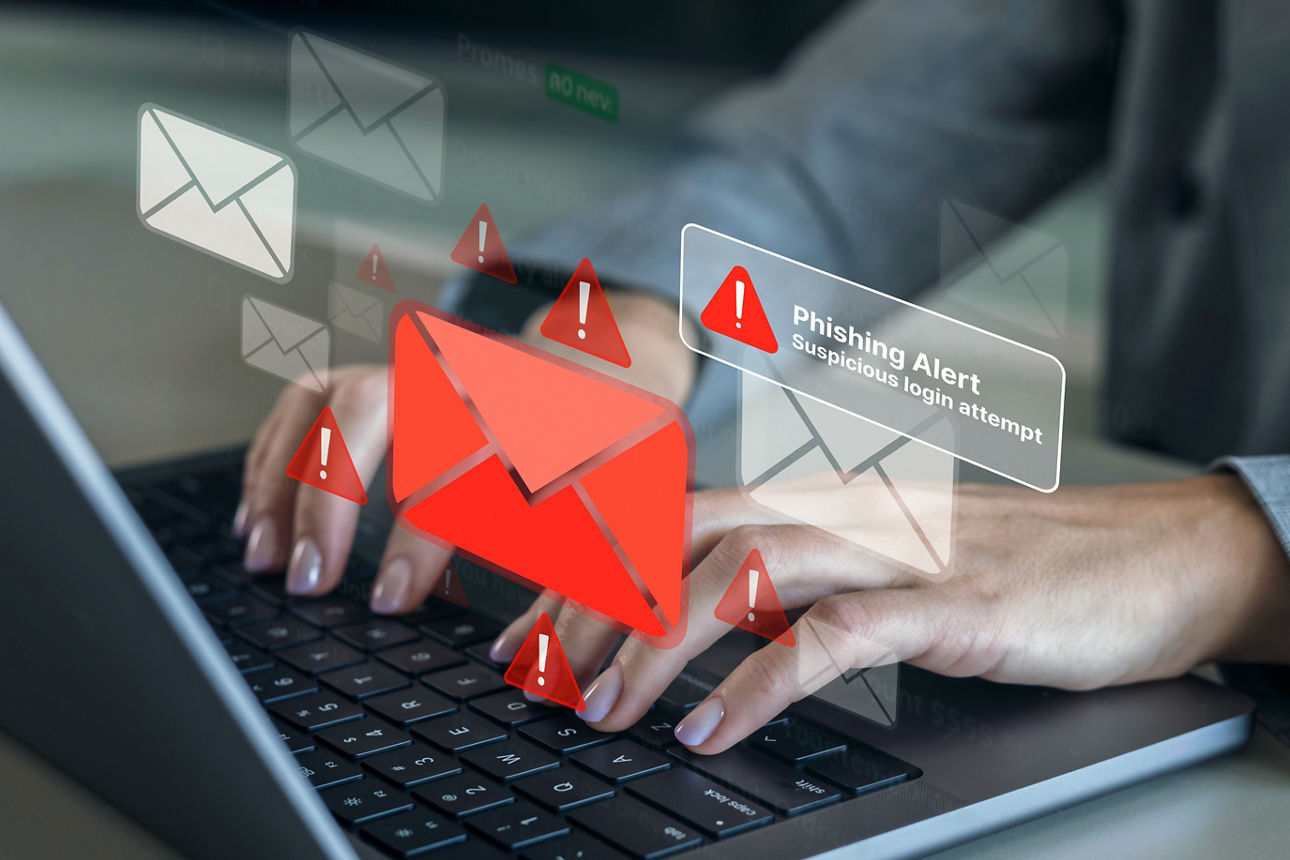 Ausschnitt einer Person vor einem Laptop mit digital angezeigter Phishing-Angriffswarnung.