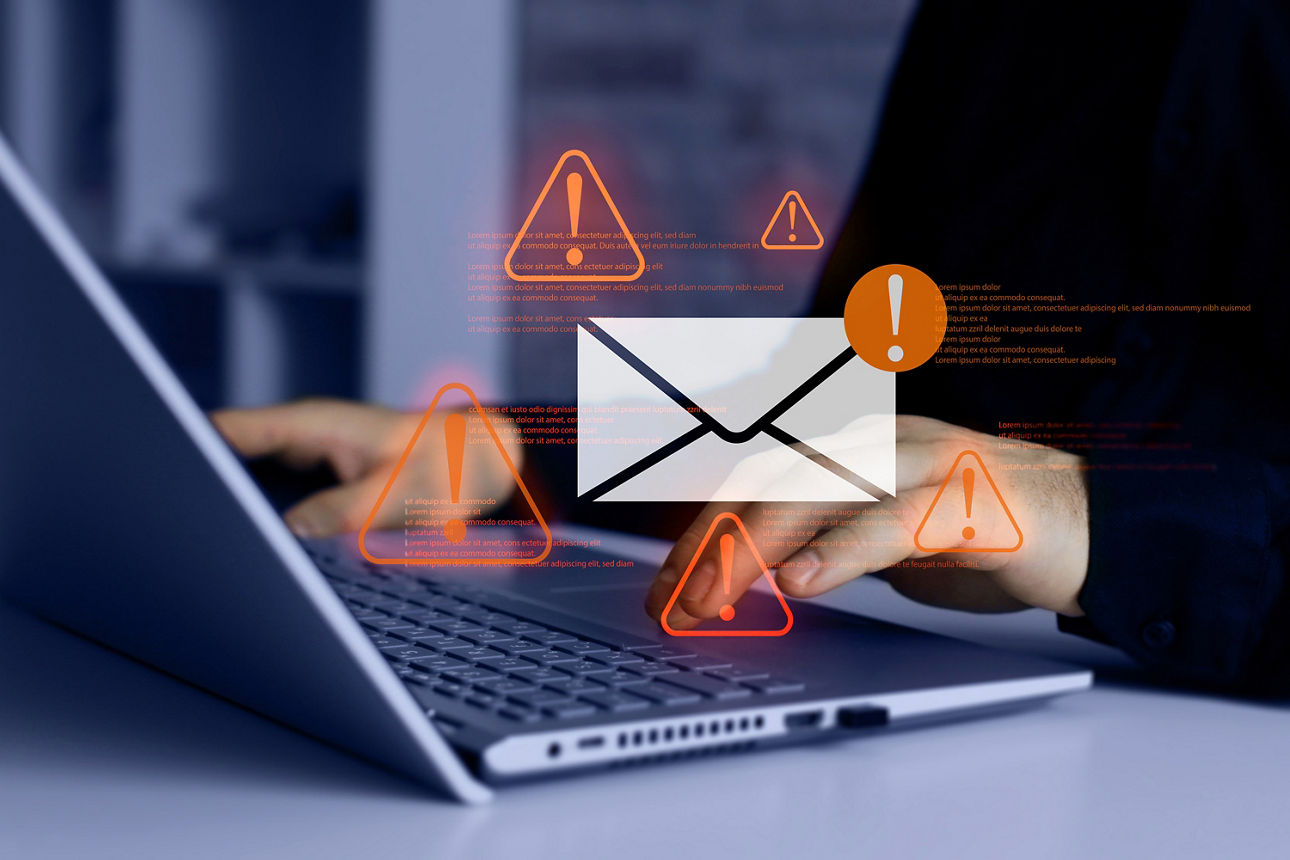 Person arbeitet an einem Laptop; eingeblendetes E-Mail-Symbol und mehrere Warnsymbole über der Tastatur.