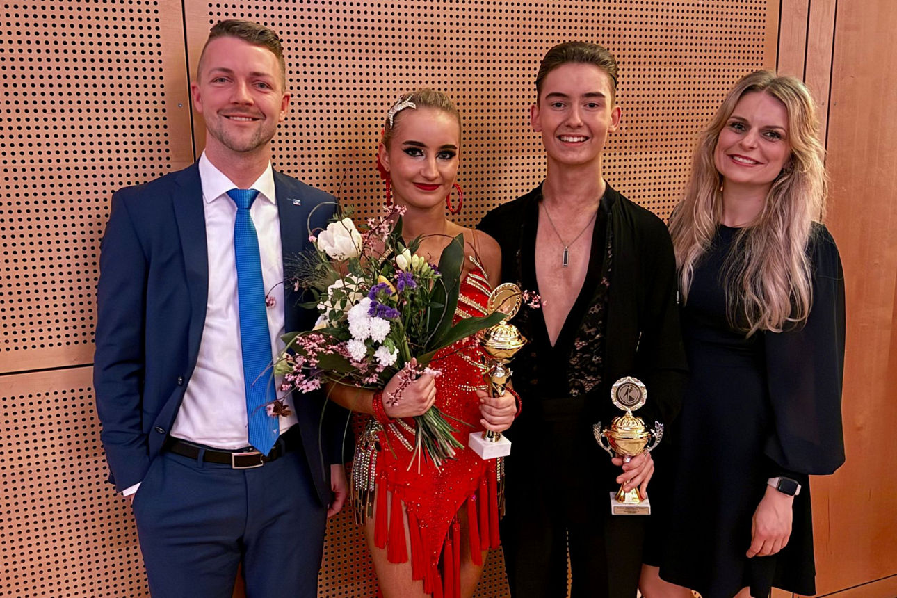 Vier Personen lächeln in die Kamera, das Paar in der Mitte festlich gekleidet mit Blumen und Pokalen