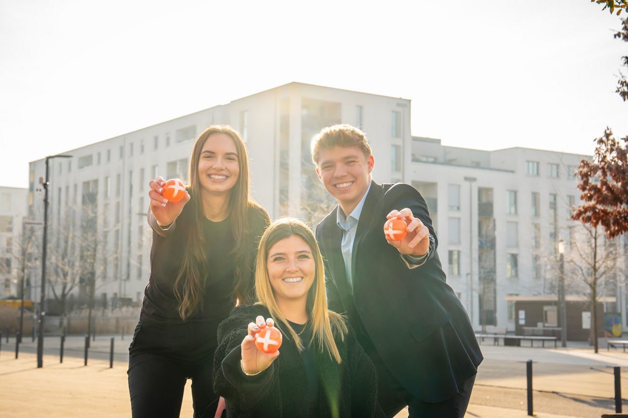 Drei Personen zeigen einen Ball mit einem Plus