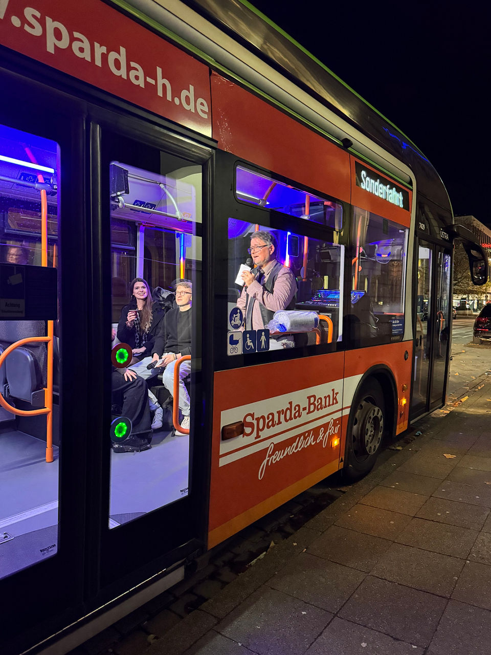 Ausschnitt einer Busansicht. Durch das Fenster sieht man einen Mann mit Mikorfon