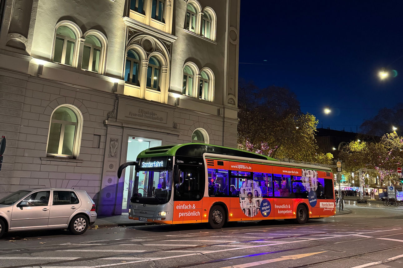 Seitenansicht eines Busses mit Sparda-Bank Werbung vor der beleuchteten Hauptfiliale in Hannover