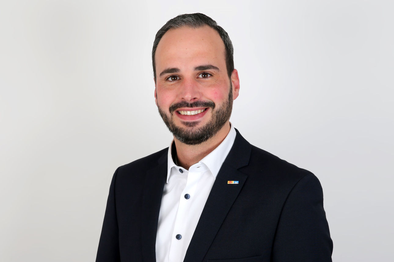 Ein lächelnder Mann in einem Anzug schaut in die Kamera.