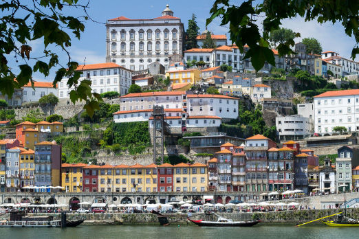 Die Stadt Porto. Bunde Häuser auf einem Berg. Im Vordergrund Wasser mit Booten.
