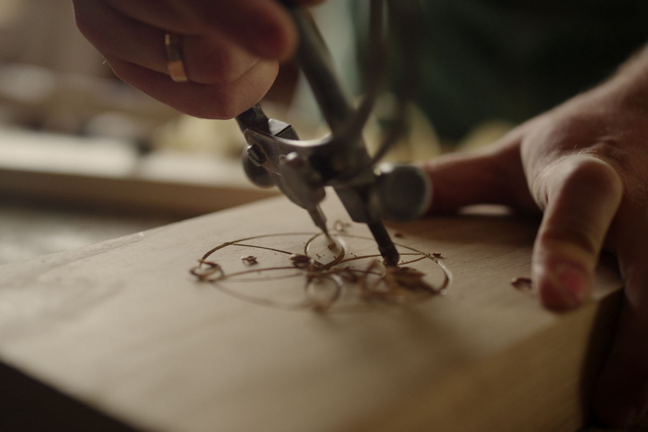 Mit einem speziellen Zirkel-Werkzeug wird ein Stück Holz per Hand graviert