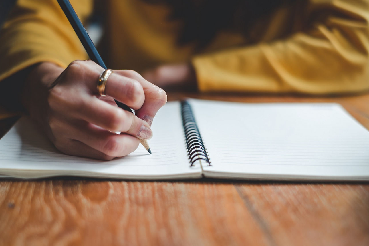 Frau schreibt mit einem Stift etwas auf ein Blatt Papier