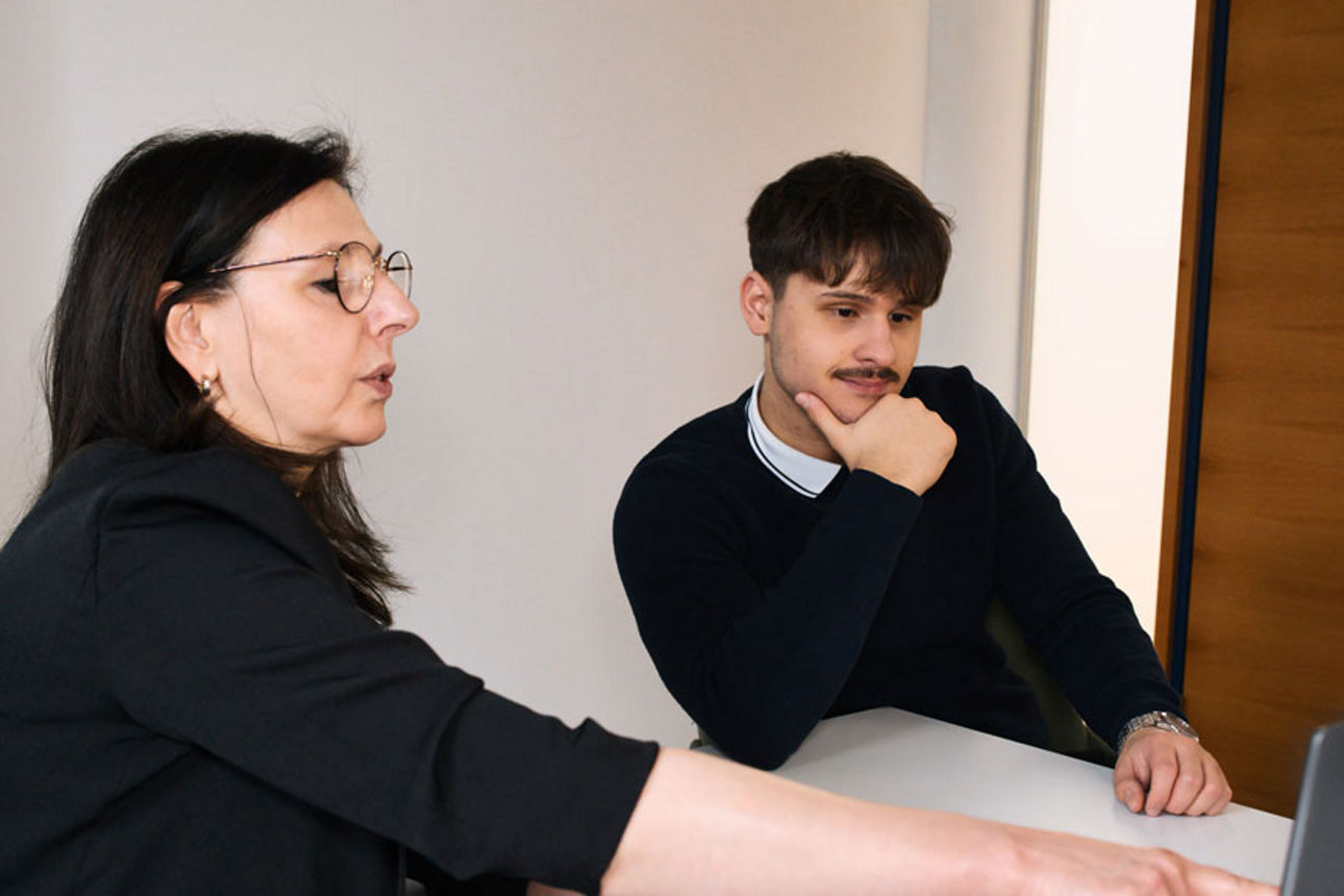 Praktikant und Frau sitzen vor PC und sie erklärt etwas