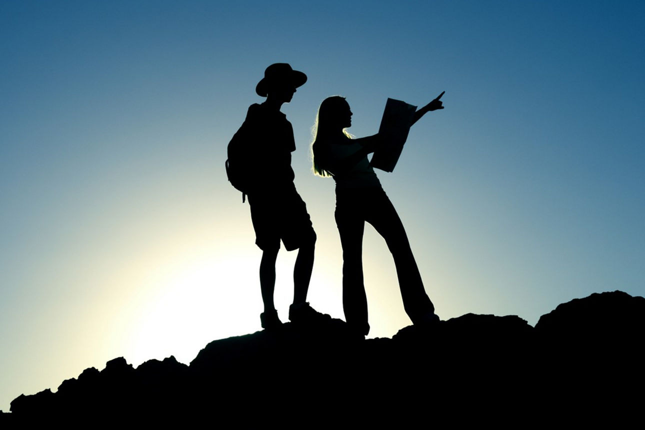 Zwei junge Menschen auf einem Felsen mit Sonne im Hintergrund