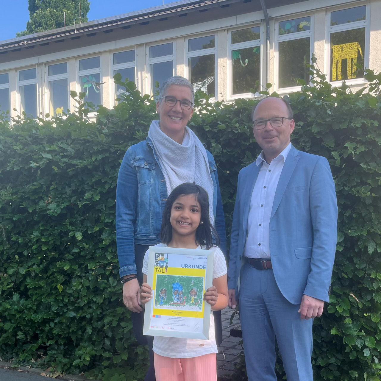 Eine Frau, ein Mann gemeinsam mit der Gewinnerin des Kunstwettbewerbs. 