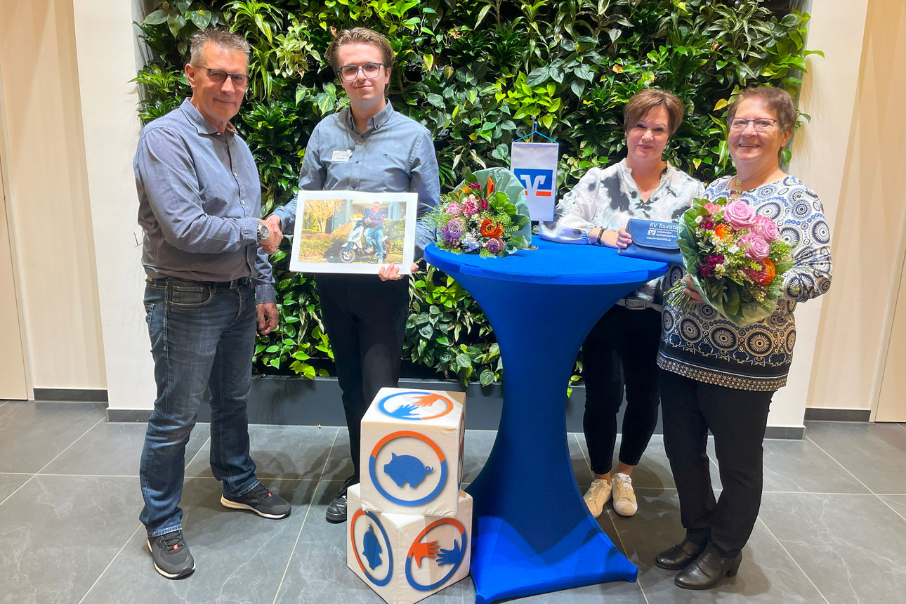 Vier Personen neben einem Stehtisch vor einer Pflanzenwand mit zwei Blumensträußen.