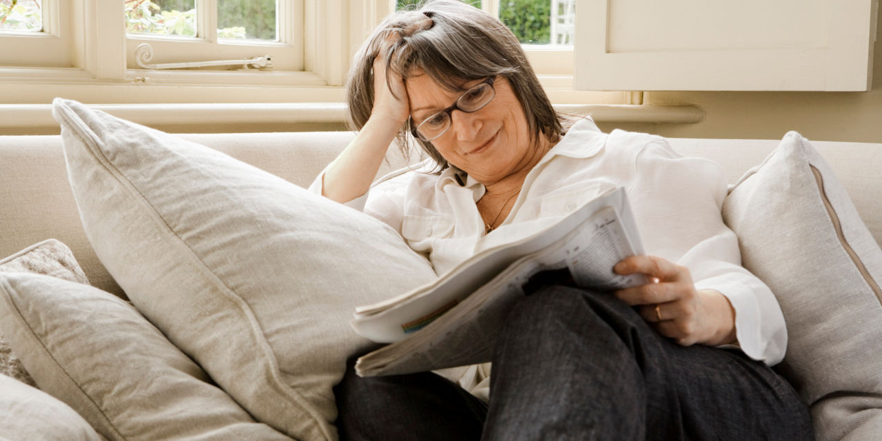  Eine Person sitzt auf einem Sofa und liest eine Zeitung, umgeben von Kissen