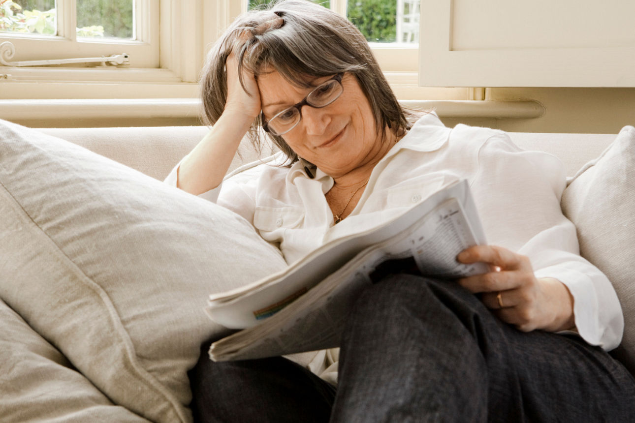  Eine Person sitzt auf einem Sofa und liest eine Zeitung, umgeben von Kissen