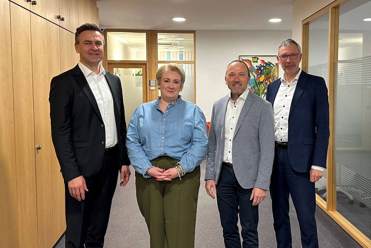 eine Frau und drei Männer in einem Bürogebäude blicken gemeinsam in die Kamera