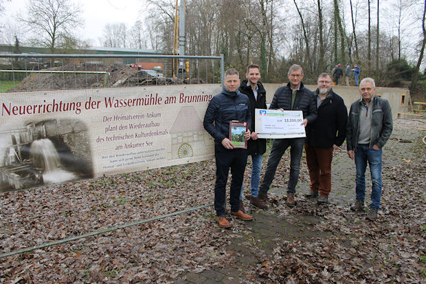 Eine Gruppe von fünf Männern steht vor einem Transparent mit der Aufschrift "Neureichung der Wassermühle am Brunning".
