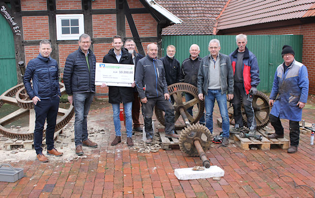 Eine Gruppe von Männern steht vor einem Backsteingebäude und hält einen großen Scheck über 13.200,00 Euro in der Hand.
