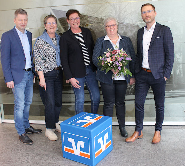 Eine Gruppe von fünf Personen steht vor einer Glastür und lächelt in die Kamera.