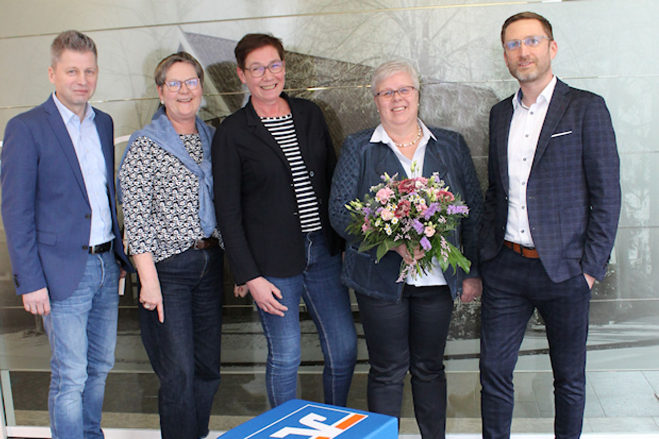 Eine Gruppe von fünf Personen steht vor einer Glastür und lächelt in die Kamera.