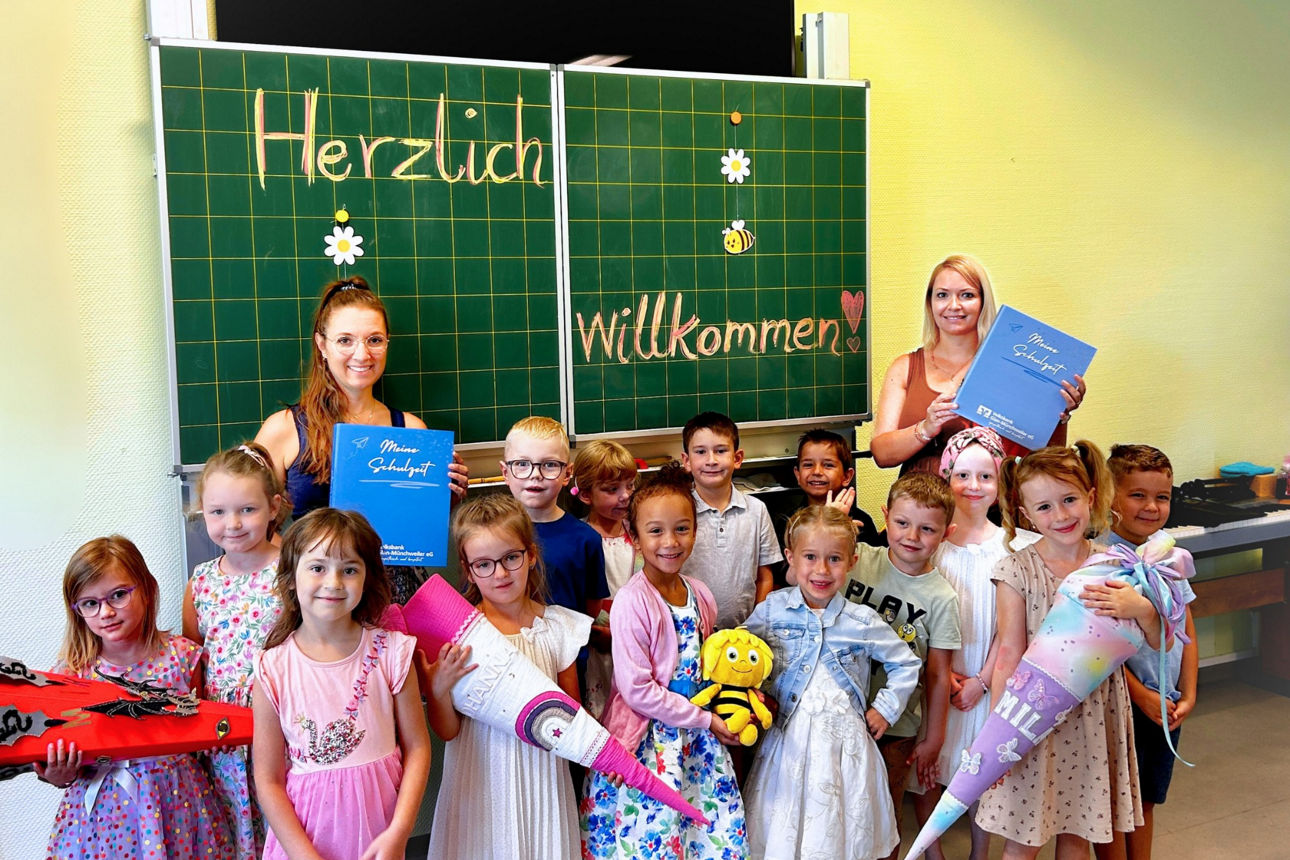 Eine Schulklasse vor einer Klassentafel mit Schultüten und ihren beiden Lehrerinnen. 