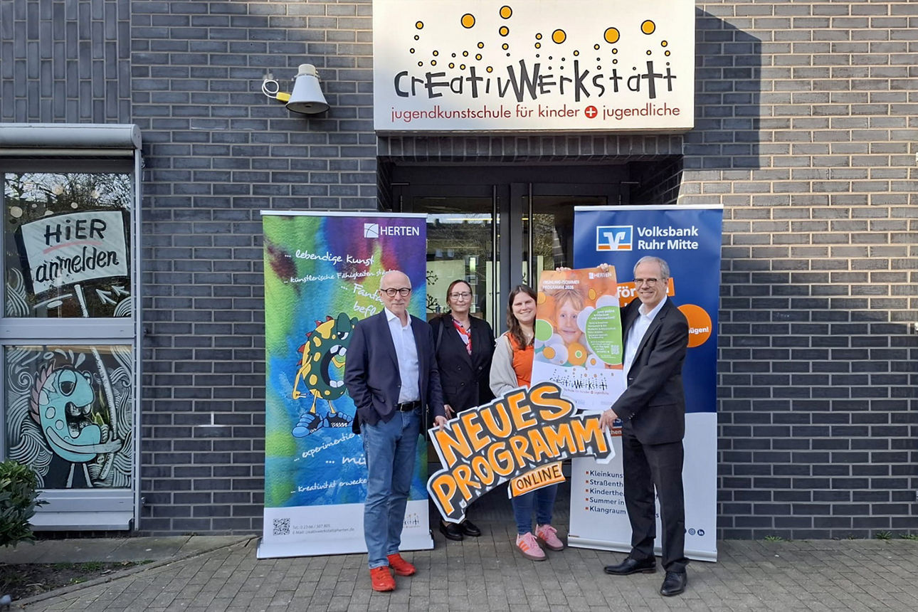 Vor dem Gebäude der Creativwerkstatt Herten stehen 4 Personen. Von links nach rechts: Hertens Bürgermeister Fred Toplak, Marion Rühl von der Volksbank Ruhr Mitte, Linda Koitka von der CreativWerkstatt und Ingo Abrahams, unser Vorstandssprecher. Im Hintergrund stehen Rollups und im Vordergrund wird das neue Plakat der Creativwerkstatt hochgehalten.