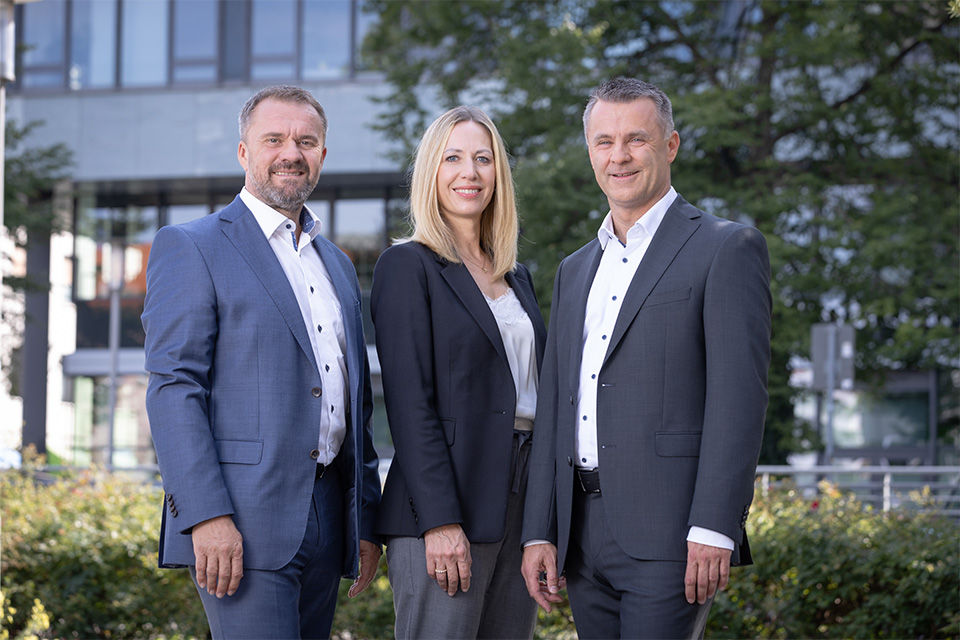 Die drei Vorstände der PSD Bank Nürnberg stehen nebeneinander vor der PSD Bank.