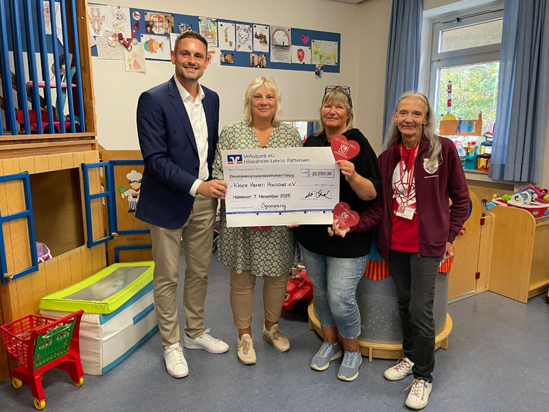 Ein Mann und drei Frauen stehen in einem Spielzimmer in der MHH und halten einen Überreichungsscheck in der Hand