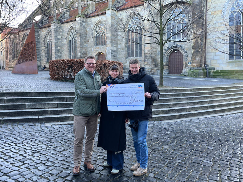 Drei Personen vor der St. Andreas Kirche in Hildesheim bei der Scheckübergabe