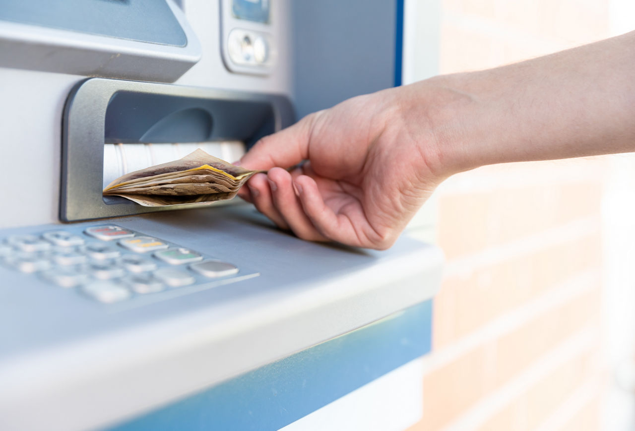 Das Bild zeigt eine Hand, die Bargeld aus einem Geldautomaten nimmt.