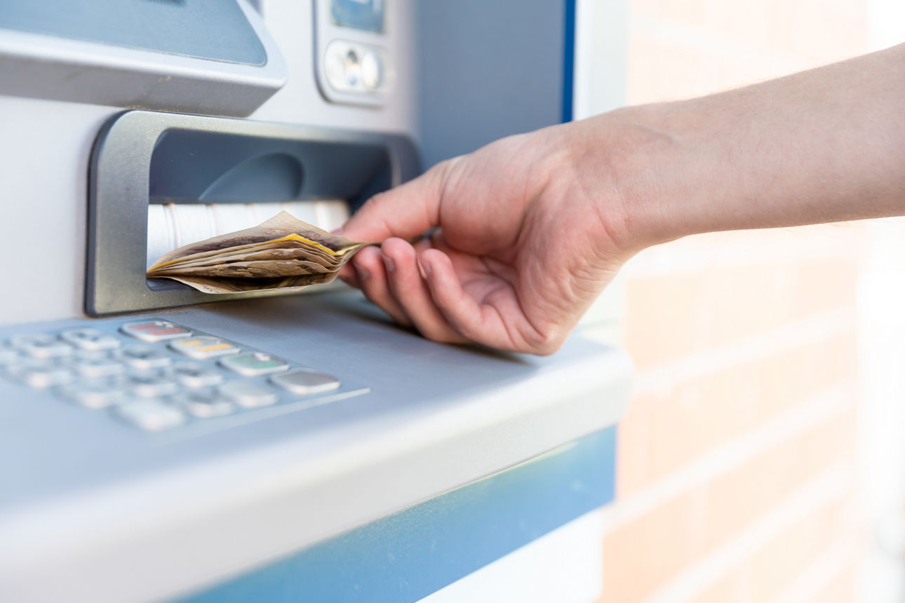 Das Bild zeigt eine Hand, die Bargeld aus einem Geldautomaten nimmt.