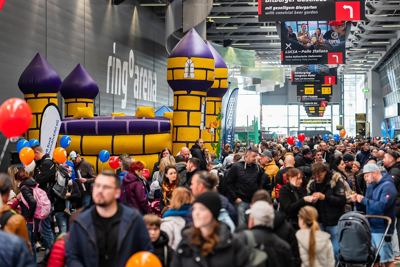 Familien mit Kindern beim Familientag am Nürburgring in der ring°arena, bunte Hüpfburg und Luftballons, Banner „Nürburgring“