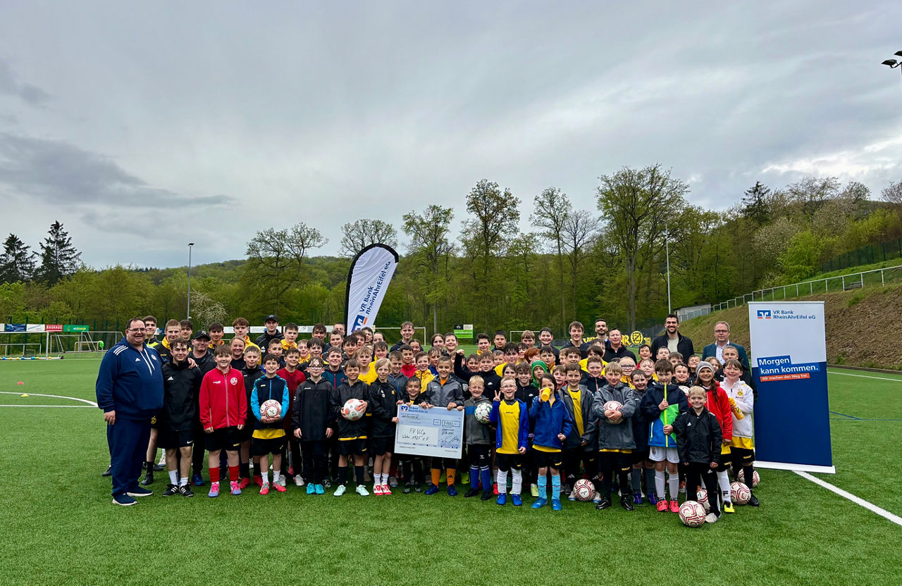 Eine große Gruppe von Erwachsenen und Kindern stehen auf einem Fußballfeld zusammen.
