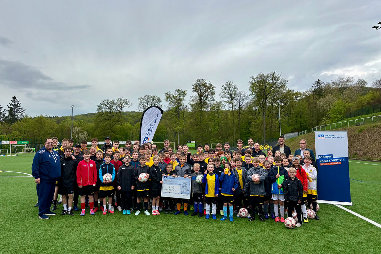 Eine große Gruppe von Erwachsenen und Kindern stehen auf einem Fußballfeld zusammen.