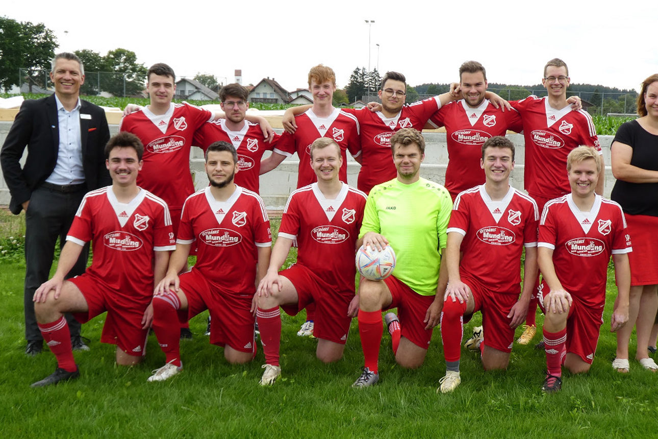 Fußballmannschaft steht aufgereicht auf dem Sportplatz mit einem Mitarbeiter unserer Bank