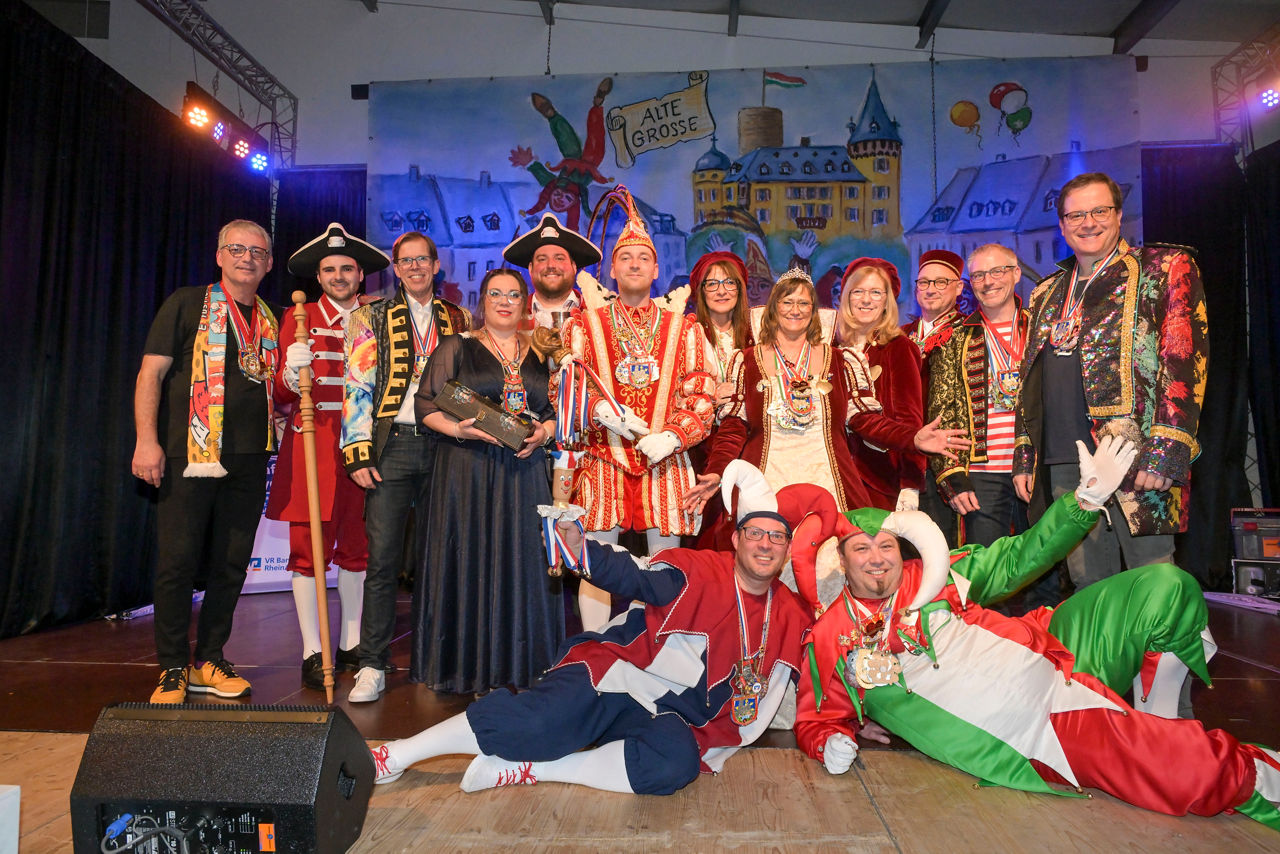 Mehrere Erwachsene stehen und sitzen in karnevalistischer Kleidung zu einem Gruppenbild zusammen.