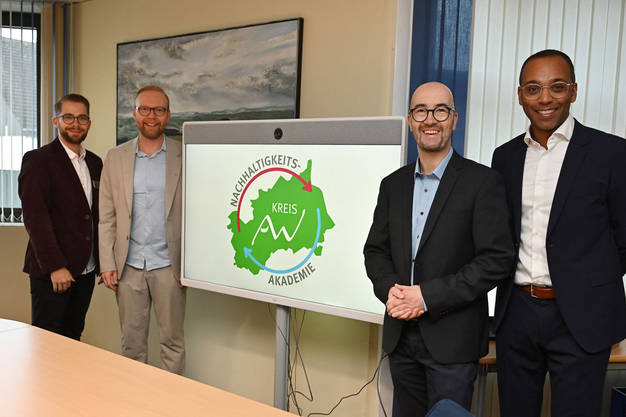 Vier Personen im Konferenzraum neben Monitor mit Logo und Text „NACHHALTIGKEITS-AKADEMIE KREIS AW