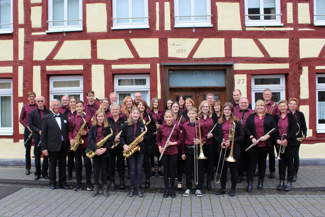 Mehrere Personen stehen mit Musikinstrumenten vor einem Fachwerkhaus zusammen.