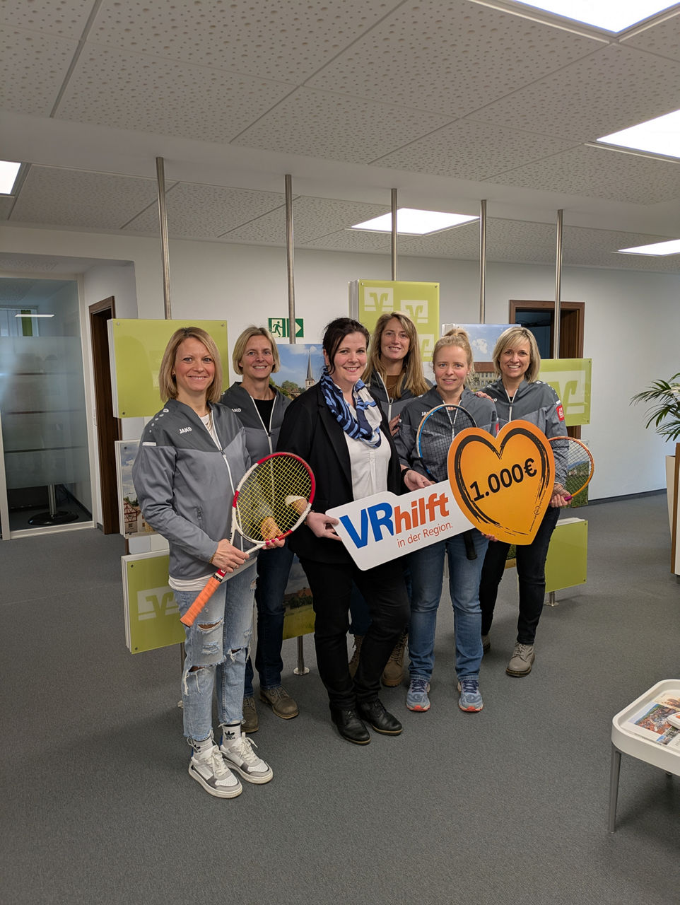 Sechs Frauen stehen in einem Büro, einige halten Tennisschläger. Es handelt sich um eine Spendenübergabe.
