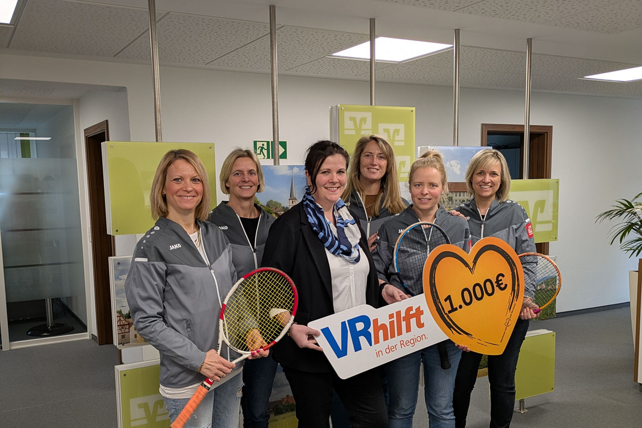 Sechs Frauen stehen in einem Büro, einige halten Tennisschläger. Es handelt sich um eine Spendenübergabe.