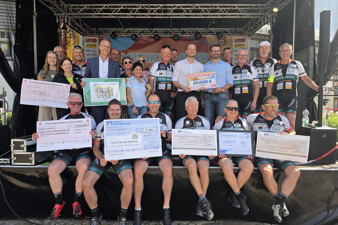 Gruppenfoto VOR-TOUR der Hoffnung: Radsportteam auf Bühne mit Spendenschecks