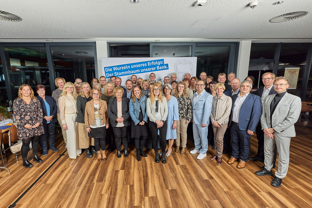 Gruppenfoto der Jubilare der VR Bank RheinAhrEifel eG vor Schild „Die Wurzeln unseres Erfolgs: Der Stammbaum unserer Bank“
