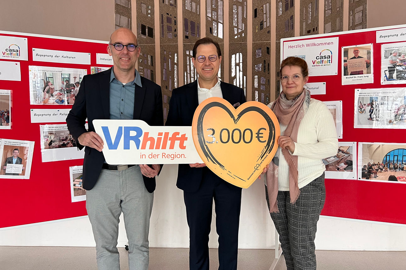 Drei Personen stehen gemeinsam vor einer Infowand und halten ein Schild mit dem Spendenbeitrag von 3.000 €.