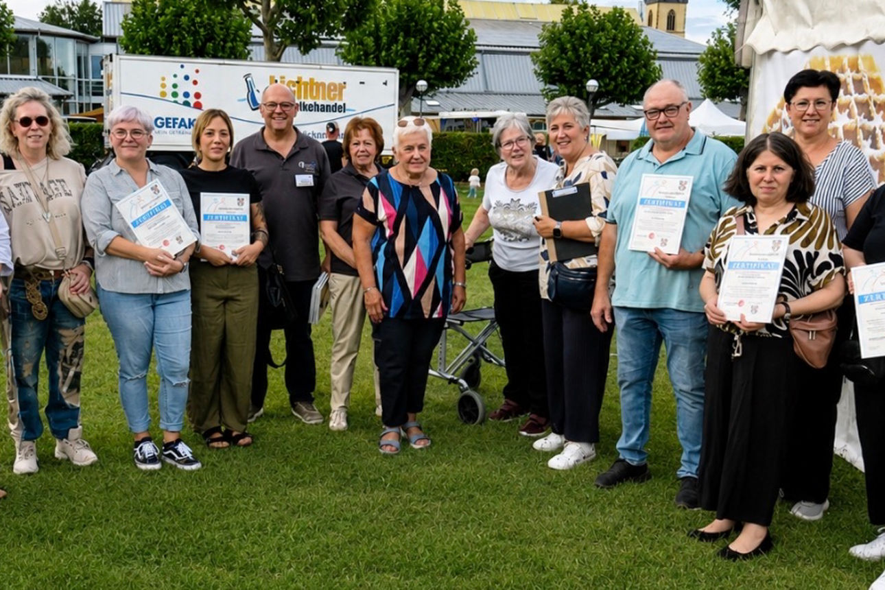 Männer und Frauen stehen in einem Halbkreis auf der Wiese und halten das Siegel des Seniorenfreundlichen Service fest.