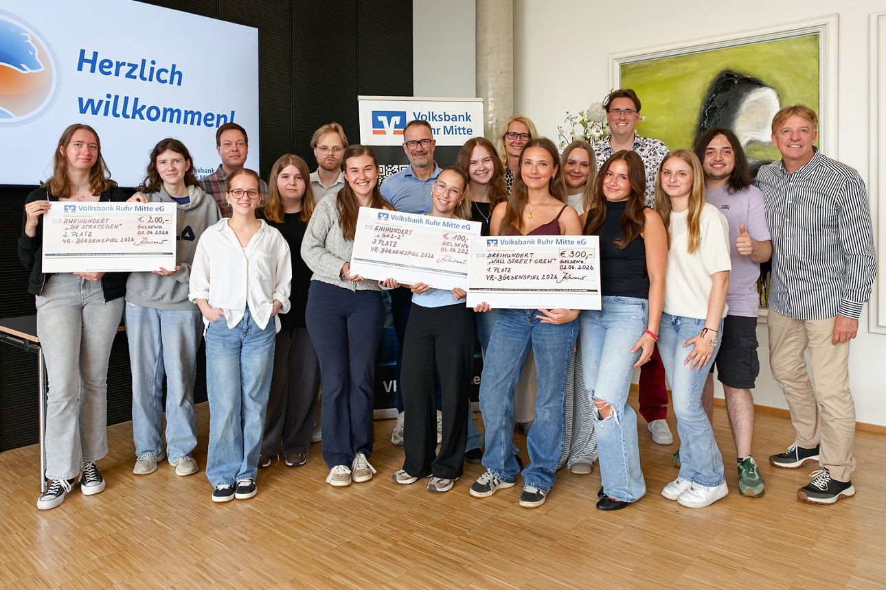 Gruppenfoto aller Teilnehmer des VR-Börsenspiels der Gesamtschule Erle aus Gelsenkirchen, inklusive dreier Lehrer und drei Vertretern der Volksbank Ruhr Mitte. Aufgenommen im Forum der Volksbank Ruhr Mitte. In der ersten Reihe werden drei große Promotionschecks in die Kamera gehalten. Alle lächeln fröhlich.