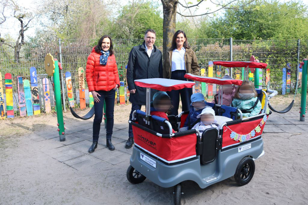 Spendenübergabe der Heidelberger Volksbank im Vordergrund sitzen mehrere Kinder im Kinderbus im Hintergrund 3 Erwachsene