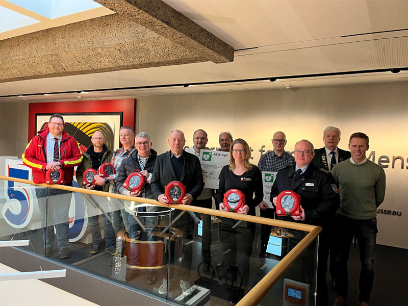 Die Vereinsverteter stehen als Gruppe zusammen und halten die gewonnenen Defibrillatoren in den Händen.