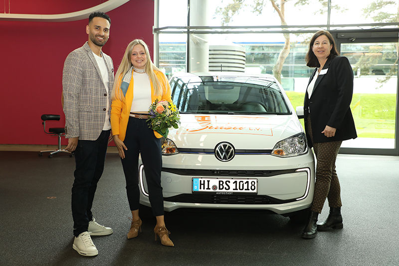 Ein Mann und eine Frau stehen lächelnd vor dem weißen eVRmobil bei der Übergabe in der Autostadt in Wolfsburg.