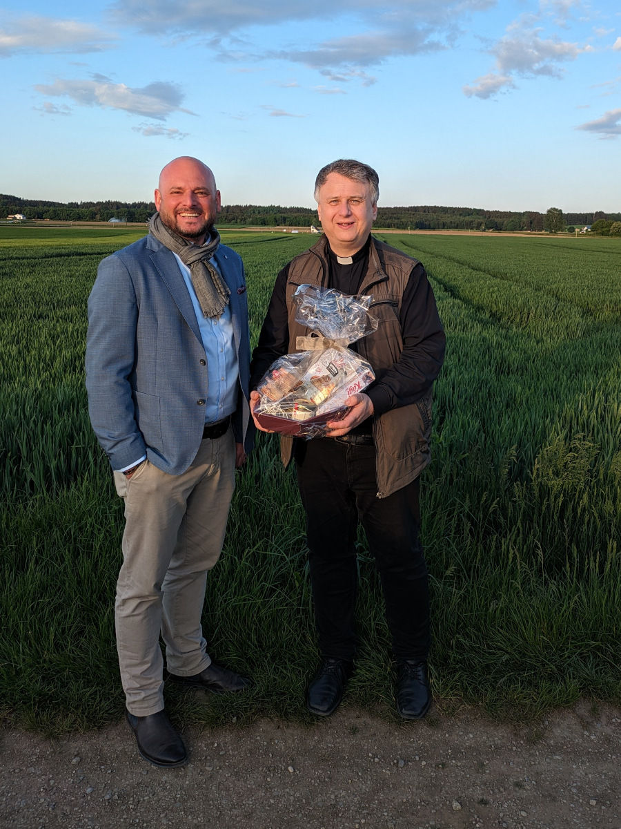 Vorstand steht mit dem Dekan mit Geschenkkorb vor einem grünen Feld